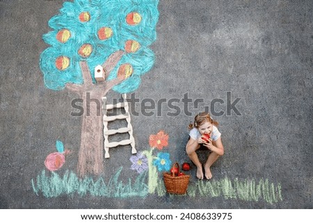 Cute little girl painting with colorful chalks apples harvest from apple tree on asphalt. Cute preschool child with having fun with chalk picture. Creative leisure for children, drawing and painting.