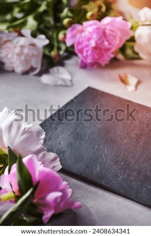 Petals and flowers of pink peonies on a gray concrete background with a black slate board and copy space for the dough. Postcard