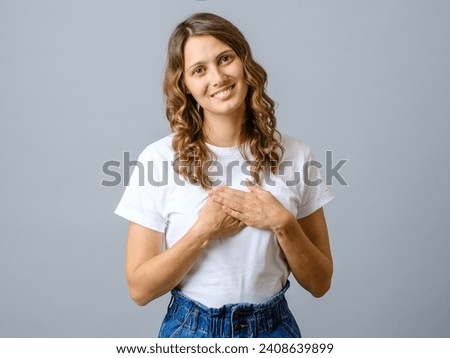 Friendly pleasant woman keeps hands on chest, touched by compliment, smiles positively over gray background Royalty-Free Stock Photo #2408639899