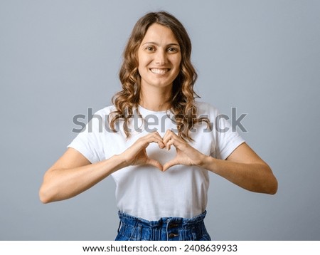 Cheerful beautiful woman making heart shape by hands isolated on a gray background