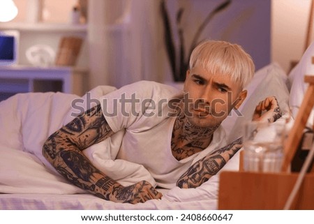 Young tattooed man watching time in bed at night