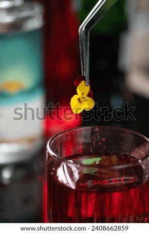 Bartender adds a delicate yellow edible flower, enhancing the Negroni cocktail with a hint of botanical charm.