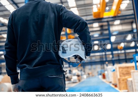 Rear view of an unrecognizable worker holding a helmet in a factory
