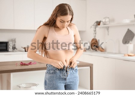 Young woman in tight jeans at home. Weight gain concept Royalty-Free Stock Photo #2408665179