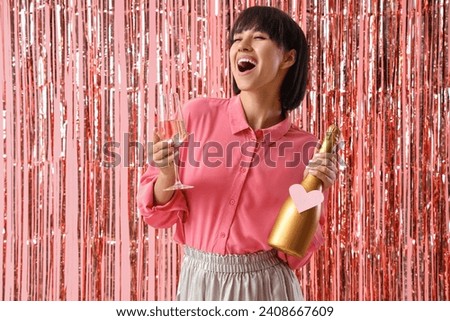 Happy young woman with bottle and glass of champagne and tinsel curtain on pink background. Valentine's day celebration Royalty-Free Stock Photo #2408667609