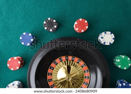 Casino roulette isolated on green felt mat with colored chips for betting around. Top view. Royalty-Free Stock Photo #2408680909