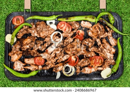 In a top angle view of assorted meat and vegetables grilling over a BBQ outdoor chicken legs on grass background.