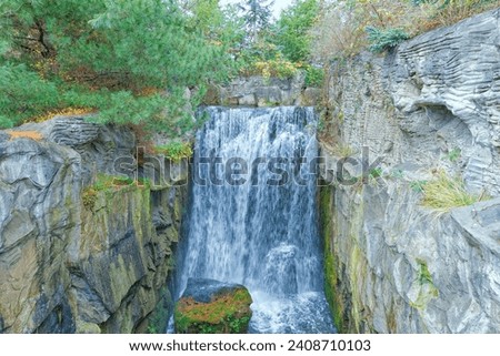 Surrounded by picturesque rocks covered with tall trees, water falls down in a continuous stream from a steep cliff.