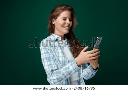 A young woman with brown hair wears a checkered blue shirt and stands on a green background with copy space