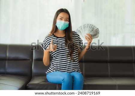 Portrait beautiful young asian woman with mask on sofa show money or cash at home Royalty-Free Stock Photo #2408719169