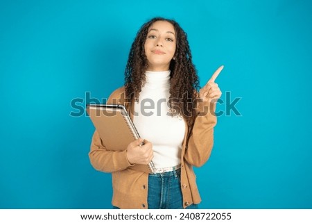 Beautiful student girl holding books wearing formal clothes smiling and looking friendly, showing number one or first with hand forward, counting down