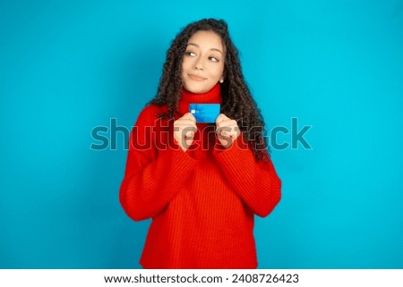 Photo of cheerful Beautiful student girl holding books wearing red sweater hold debit card look empty space