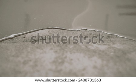 Self-leveling floor on a concrete surface close-up. Partial covering of the floor with self-leveling cement mortar. Self-leveling mixture for repairing floors in an apartment. Royalty-Free Stock Photo #2408731363