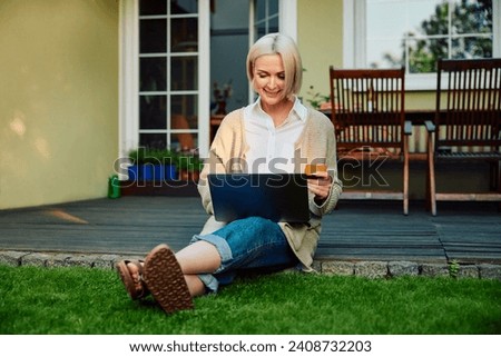 Portrait of mature woman using laptop paying with credit card sitting at backyard patio