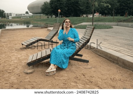 Young pretty woman model in stylish dresses talk by mobile cell phone look aside standing on summer in spring park outdoors. Urban lifestyle concept. High quality photo Royalty-Free Stock Photo #2408742825