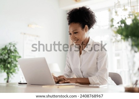 Engrossed professional woman working on her laptop in a bright, plant-filled room. Royalty-Free Stock Photo #2408768967