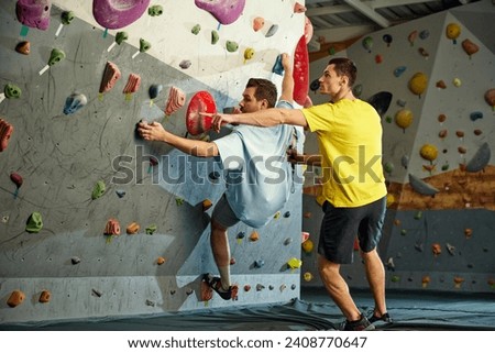 Male instructor teaching man to climb artificial wall. Man training, climbing up the artificial stones. Bouldering activity. Concept of sport, sport climbing, hobby, active lifestyle, school, course Royalty-Free Stock Photo #2408770647
