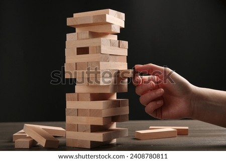 Woman playing Jenga at table against dark gray background, closeup