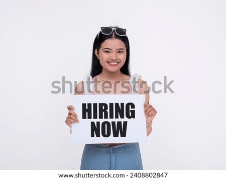 A young woman holding a sign with the words hiring now. Recruiting new employees and staff. Isolated on a white background.