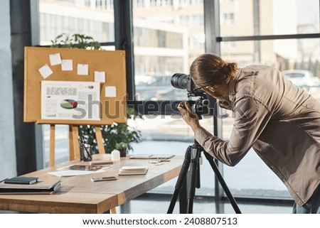 creative manager adjusting digital camera near corkboard with graphs for presentation in office