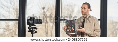 businessman showing paper with graphs and recording video blog on digital camera in office, banner