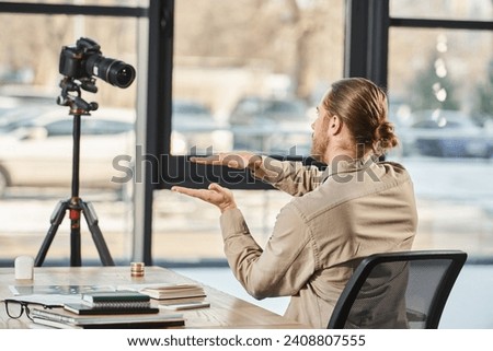 back view of entrepreneur gesturing in front of digital camera at work desk in modern office