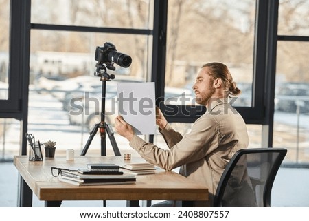 side view of manager in casual attire showing document at digital camera during video blog in office