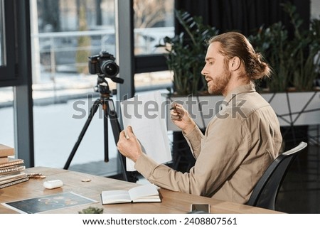 businessman in casual attire showing document at digital camera and recording video blog in office