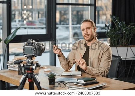 serious entrepreneur talking and gesturing in front of digital camera during video blog in office