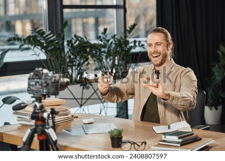 overjoyed creative businessman holding bitcoins in front of digital camera at work desk in office