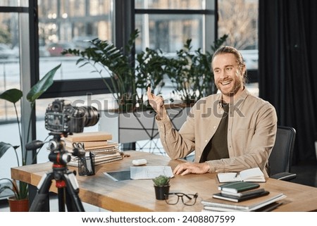 happy successful businessman talking and gesturing during video blog at work desk with notebooks