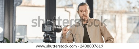 businessman talking and gesturing near digital camera during video blog in office, horizontal banner