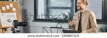 smiling businessman with laptop talking in front of digital camera in office, horizontal banner