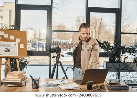 manager in casual attire adjusting laptop and digital camera near work desk in office, video blogger