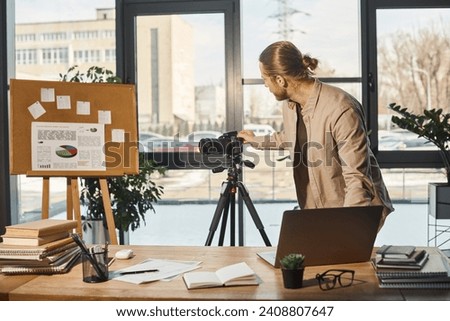 corporate manager adjusting digital camera on tripod near flip chart with graphs and office desk