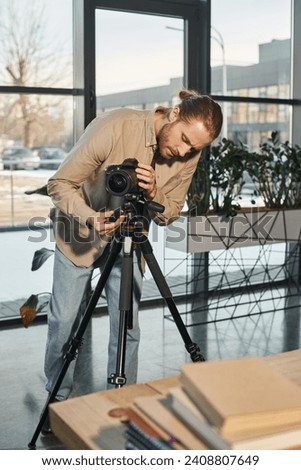 businessman in casual clothes adjusting digital camera on tripod in office, commercial marketing