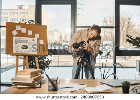 creative businessman adjusting digital camera near flip chart with analytics and work desk in office