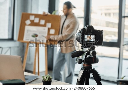 focus on digital camera and laptop near blurred businessman recording video content in office