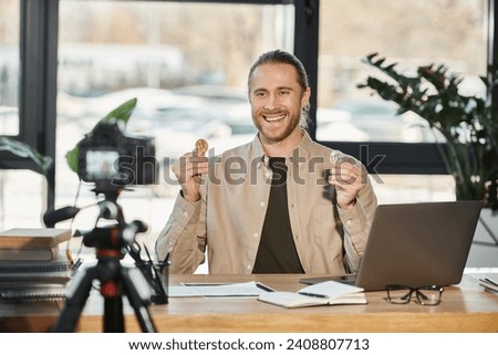 happy ambitious businessman showing bitcoins and recording video blog on digital camera in office
