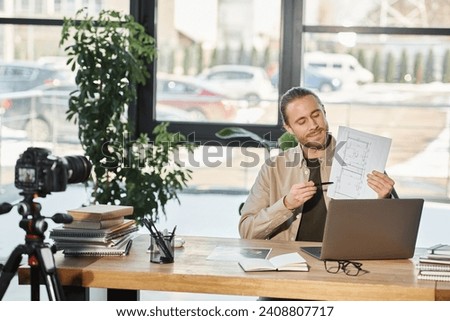 businessman in casual attire showing blueprint during video blog on laptop near digital camera