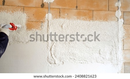 Industrial application of solution to the wall through a hose. Applying putty using a machine. Plasterers use and operate mortar spraying equipment, mortar spraying machine. Royalty-Free Stock Photo #2408821623