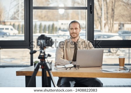 successful entrepreneur sitting at work desk in front of digital camera during video blog in office