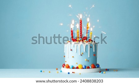 Colorful celebration birthday cake with colorful birthday candles and sparklers against a blue background Royalty-Free Stock Photo #2408838203
