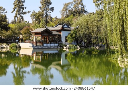 a gorgeous summer landscape in a Chinese garden with a green lake and lush green trees reflecting off the water and blue sky at Huntington Library and Botanical Gardens in San Marino California USA