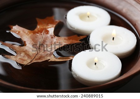 Tree white candles floating with leaf on water in bowl