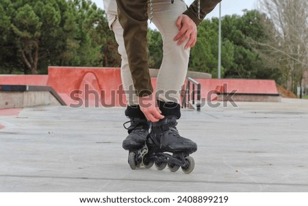 Young white guy with roller skates in a skate park in the background, half length, standing, crouching, with sweatshirt and trees in the background, unrecognizable, front view