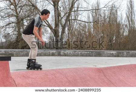 Young white guy with black roller skates in a skate park, dark hair, no helmet, going down a ramp, focused, full view. Copy space