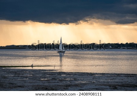A late afternoon picture of sailing boats in calm water.  Grey clouds of an approaching storm are gathering over the orange sky at sunset.