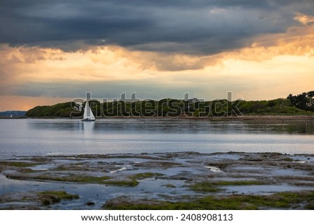 A late afternoon picture of sailing boats in calm water.  Grey clouds of an approaching storm are gathering over the orange sky at sunset.