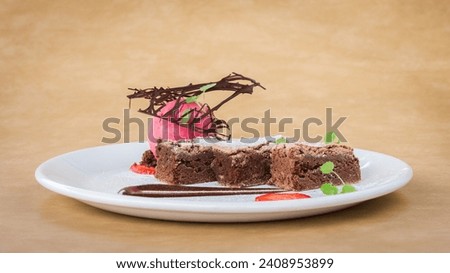 Chocolate brownie dessert with raspberry ice cream and strawberry slices on a white plate with light brown background